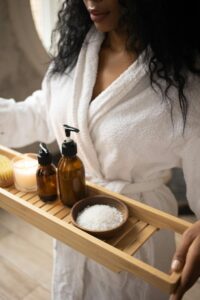 A woman in a bathrobe holds a tray of natural spa products, focusing on self-care.